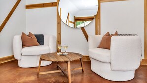 Una habitación acogedora con dos sillones blancos, una mesa redonda de madera con vasos, y un espejo en la pared.