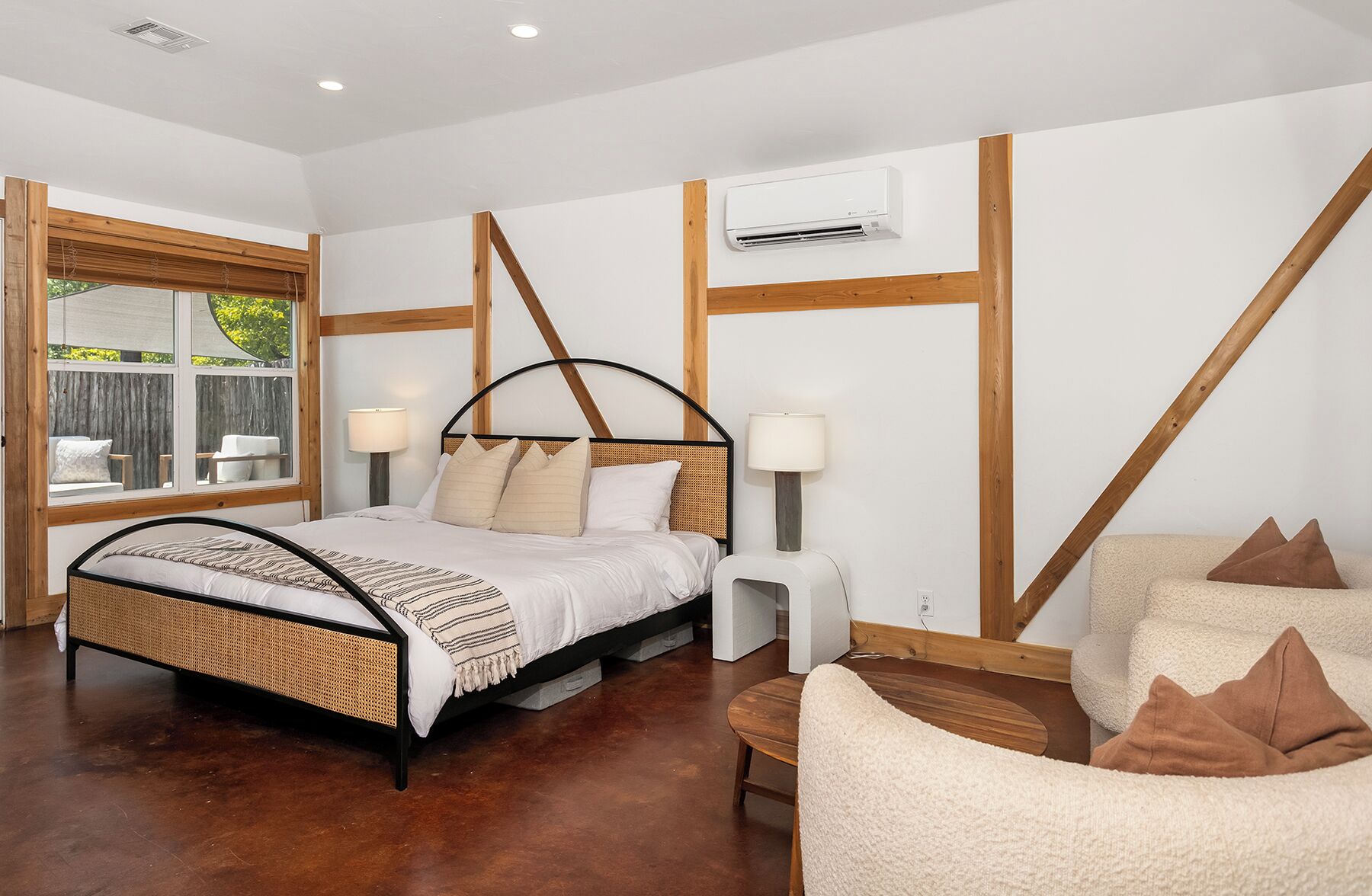 Une chambre à coucher avec un lit, des lampes de chevet, une fenêtre, un plafond en bois et un climatiseur fixé au mur.
