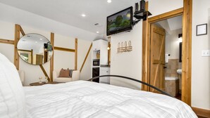 Un dormitorio con una cama, un televisor montado en la pared, una puerta de madera y una mesita de noche con lámpara.