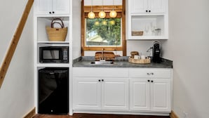 Una cocina compacta con armarios blancos, microondas integrado, un lavabo y una cafetera.