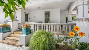 A covered porch with a white railing, steps leading up to a door, and potted plants.