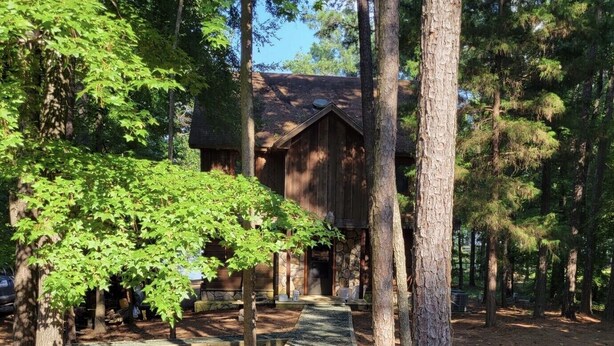 Un bâtiment rustique en bois, entouré d’arbres, avec un chemin de gravier menant à l’entrée.