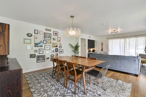 A modern living room with a dining area, featuring a wooden dining table, chairs, and a patterned rug.