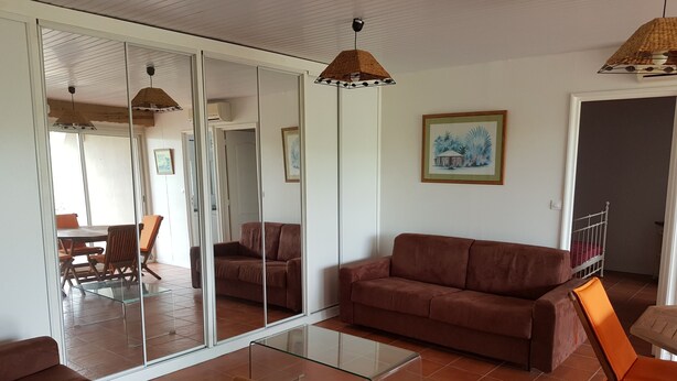 Ein Wohnzimmer mit einem braunen Sofa, einem Glastisch und einem Essbereich mit orangefarbenen Stühlen.