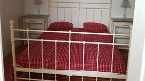 Ein Bett mit weißem Metallgestell und rot-karierter Bettwäsche, zwei Nachttische mit Lampen und eine Hängelampe.