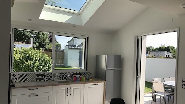 A modern kitchen with a skylight, a refrigerator, and a dining area with a table and chairs. - New house with beautiful sea view (Groix)
