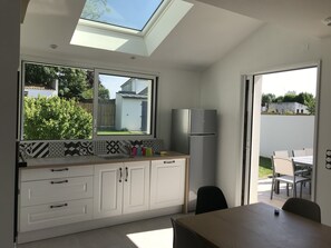 A modern kitchen with a skylight, a refrigerator, and a dining area with a table and chairs. - New house with beautiful sea view (Groix)