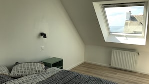 A bedroom with a sloped ceiling, a skylight, a radiator, and a bedside table. - New house with beautiful sea view (Groix)