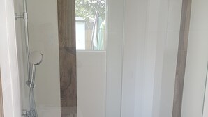 A modern bathroom with a glass-enclosed shower, a wooden accent wall, and a white bathtub. - New house with beautiful sea view (Groix)