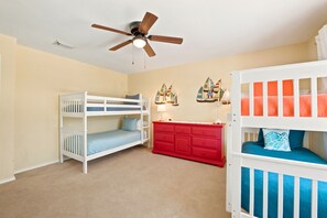 A child’s room with bunk beds, a ceiling fan, a red dresser, and sailboat wall art.