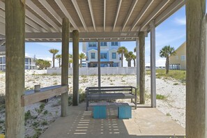 A beachside pavilion with a bench and picnic table, wooden posts, and a view of a building in the background.