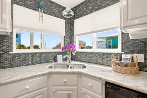 Una cocina moderna con encimera de granito, pileta de acero inoxidable y salpicadero de baldosas blancas y negras. Se ve una ventana con vistas a edificios cercanos y un colgador con luz.