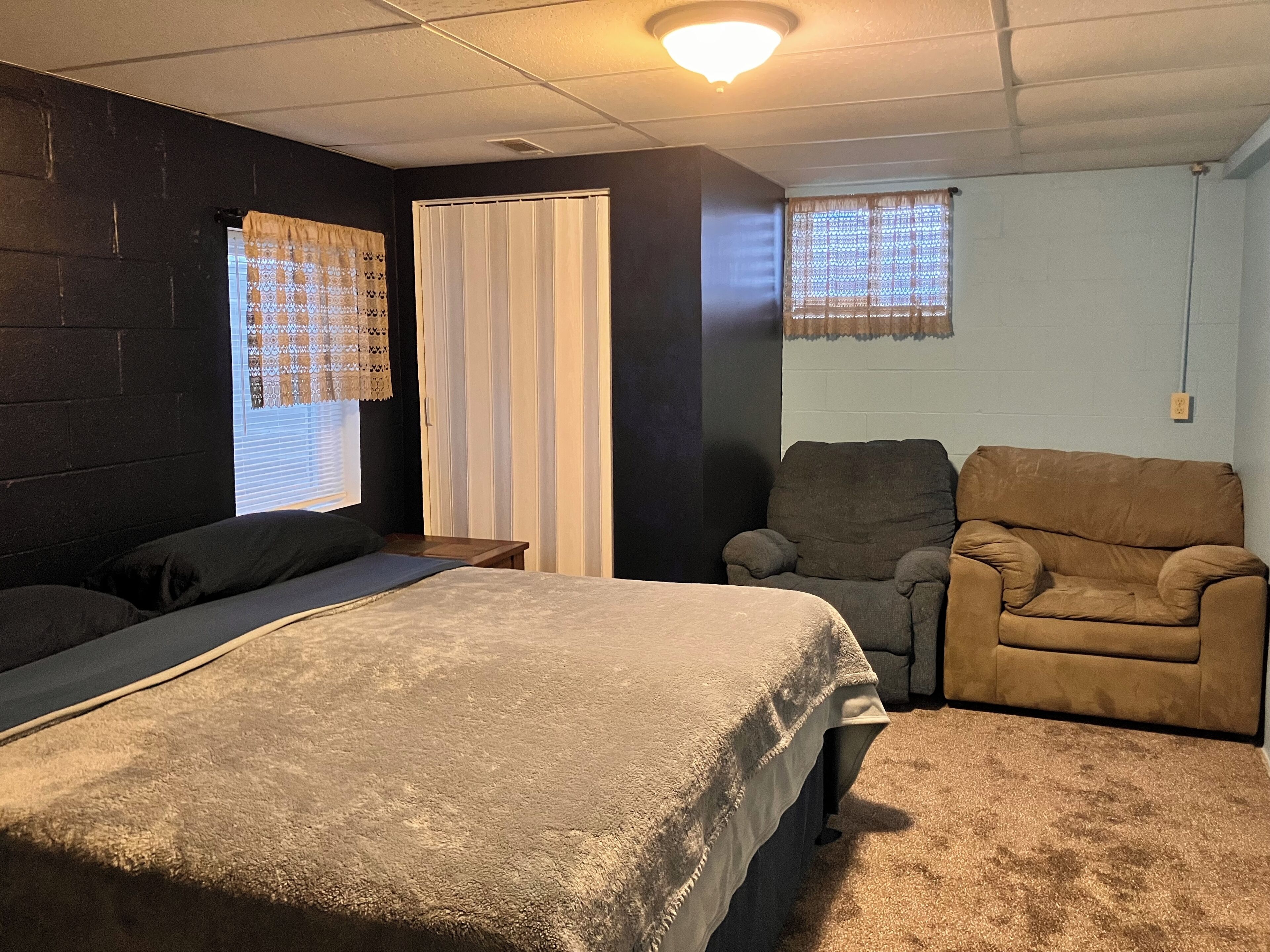 A room with a bed, two armchairs, a window with a curtain, and a door.