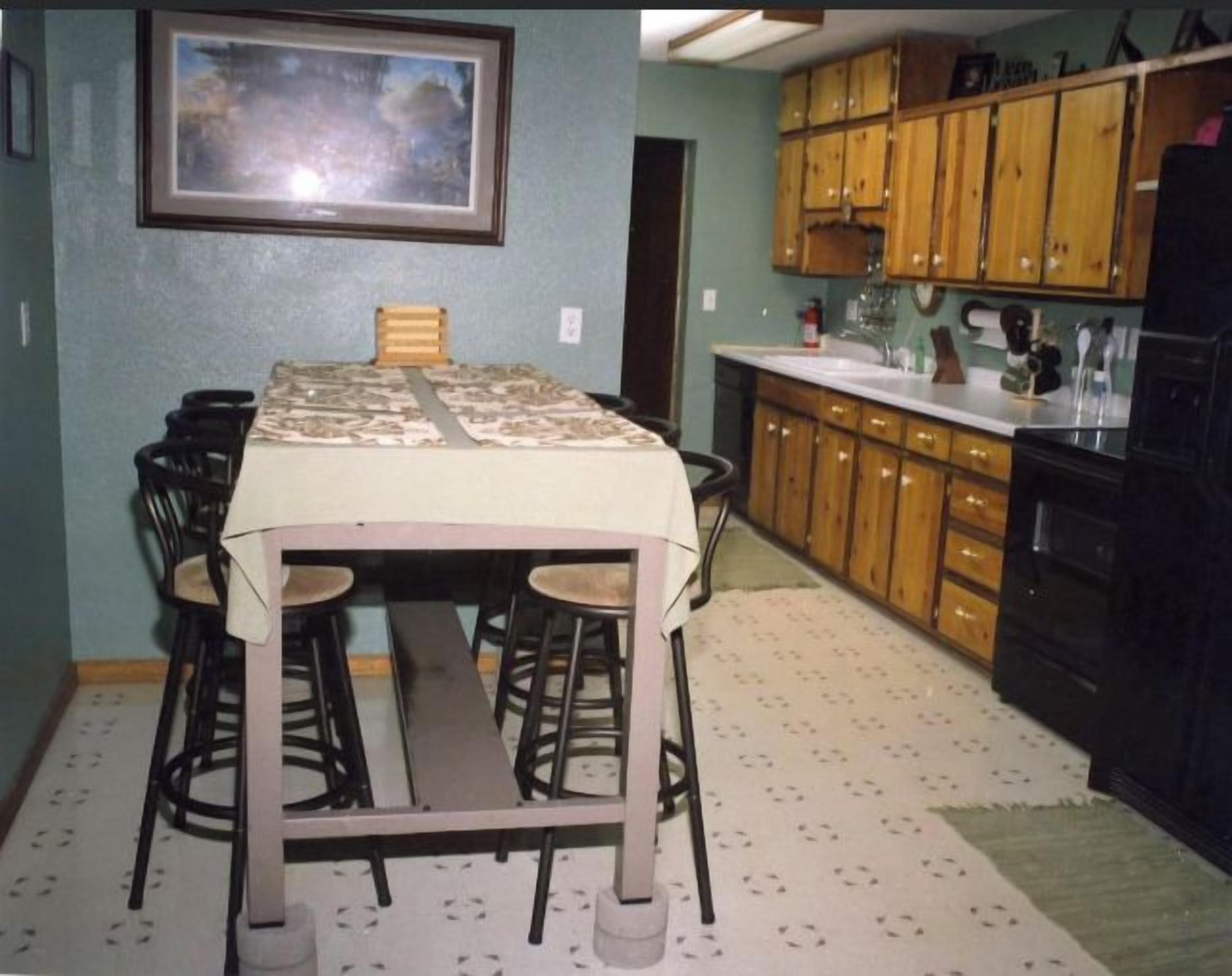 Une cuisine de taille réduite avec des meubles en bois, une table à manger avec des chaises et un tableau encadré au mur.