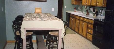 A compact kitchen with wooden cabinets, a dining table with chairs, and a framed picture on the wall.