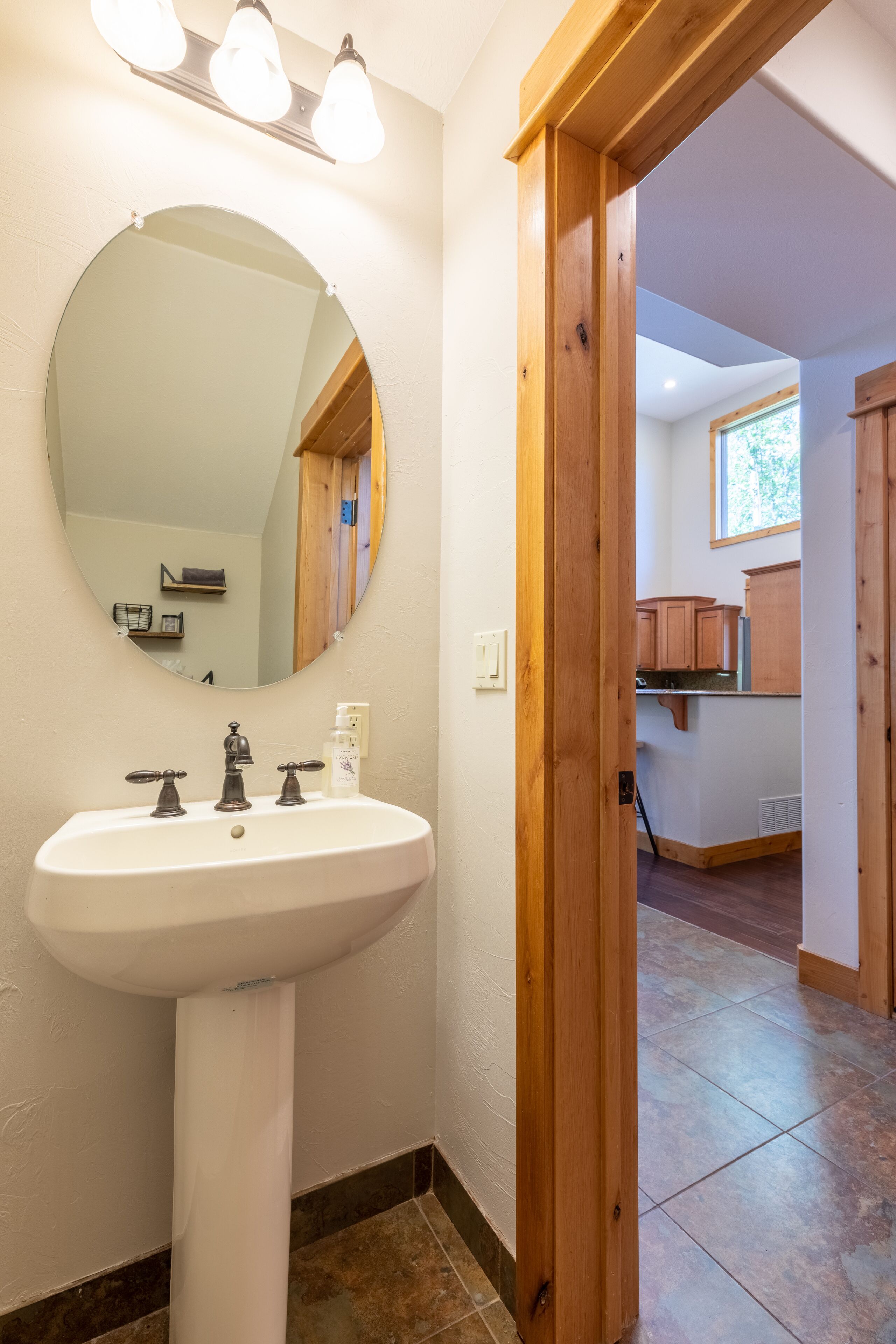 Une salle de bain avec un lavabo blanc, un miroir rond et des poutres en bois.