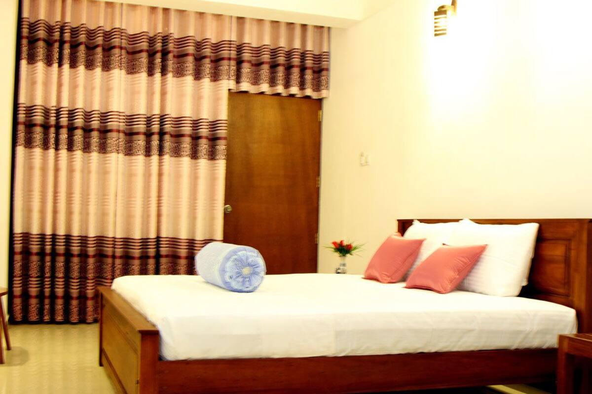 A neatly made bed with a wooden headboard, a bedside table, and a window with curtains.