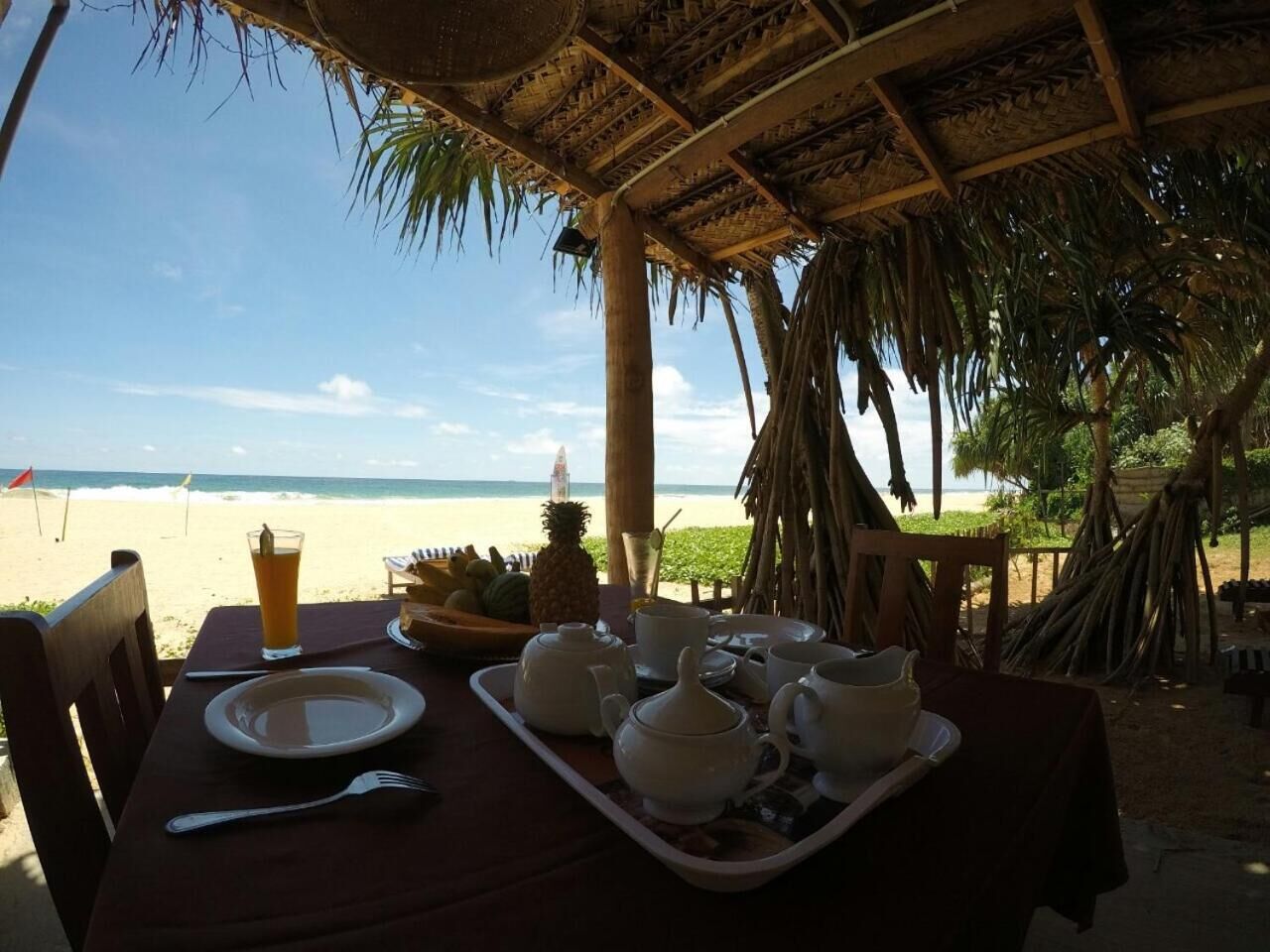 A table set for breakfast with a view of the beach, including a tray with teapots, cups, and a pineapple.