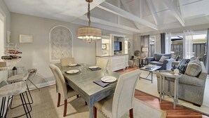 Un comedor amplio con una mesa larga, sillas y una araña. Hay una sala de estar con un sofá y una mesa de centro.