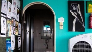A hallway with a teal wall, a white air conditioner, and a door leading to a bathroom. - Wanderthirst Hostel (Kathmandu)
