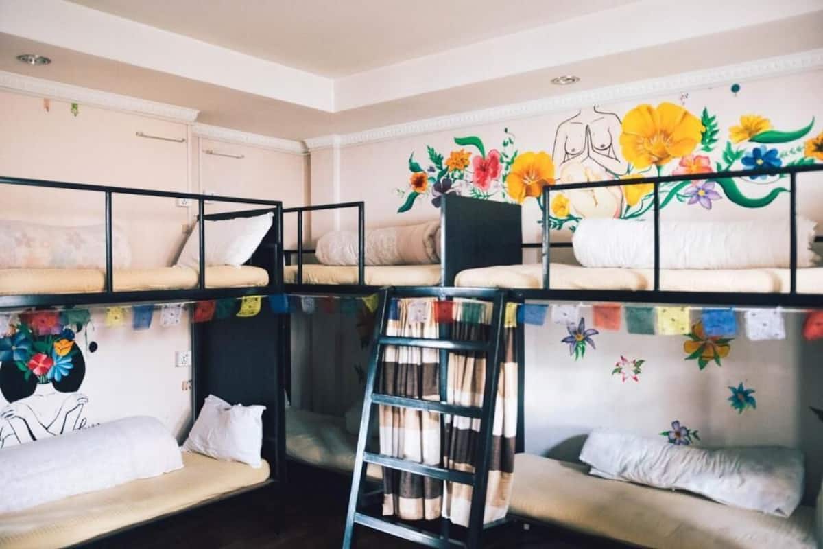 A dormitory room with bunk beds, a ladder, and a mural with floral and abstract designs.