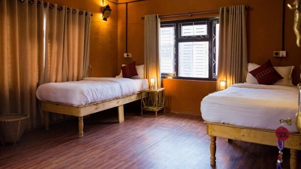 A room with two beds, wooden flooring, a window with curtains, and a wall-mounted light fixture. - Wanderthirst Hostel (Kathmandu)