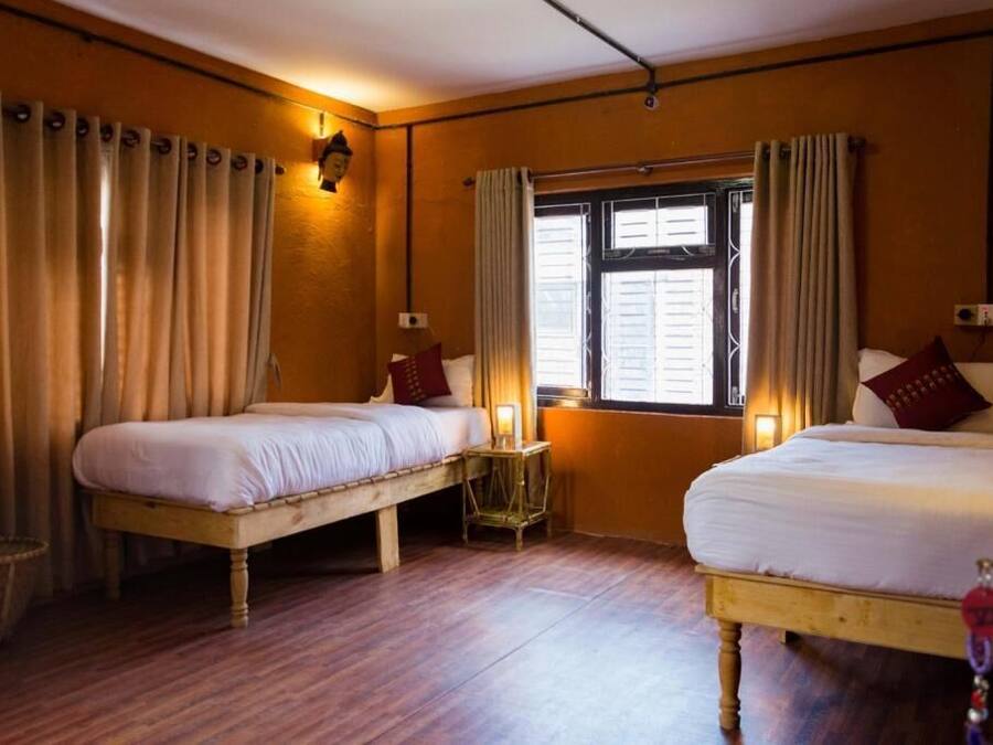 Habitación con dos camas, suelo de madera, ventana con cortinas e iluminación empotrada en la pared.