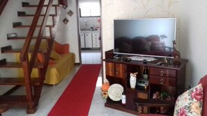 Un salon avec un téléviseur, des meubles en bois, une moquette rouge et un escalier.