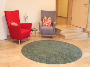 A room with two armchairs, one red and one grey, both with floral cushions, a small table with a vase of flowers, and a large green rug. - Double room small (with balcony) - Brewery-Gasthof Pfister (Eggolsheim)