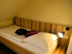Een eenpersoonsbed met houten hoofdbord, wit beddengoed en een bedlampje.