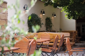 An outdoor seating area with wooden tables and chairs, surrounded by a stone wall and potted plants. - Double room small (without balcony) - Brewery-Gasthof Pfister (Eggolsheim)