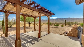 A covered outdoor area with a wooden pergola, a concrete floor, and a view of desert mountains.