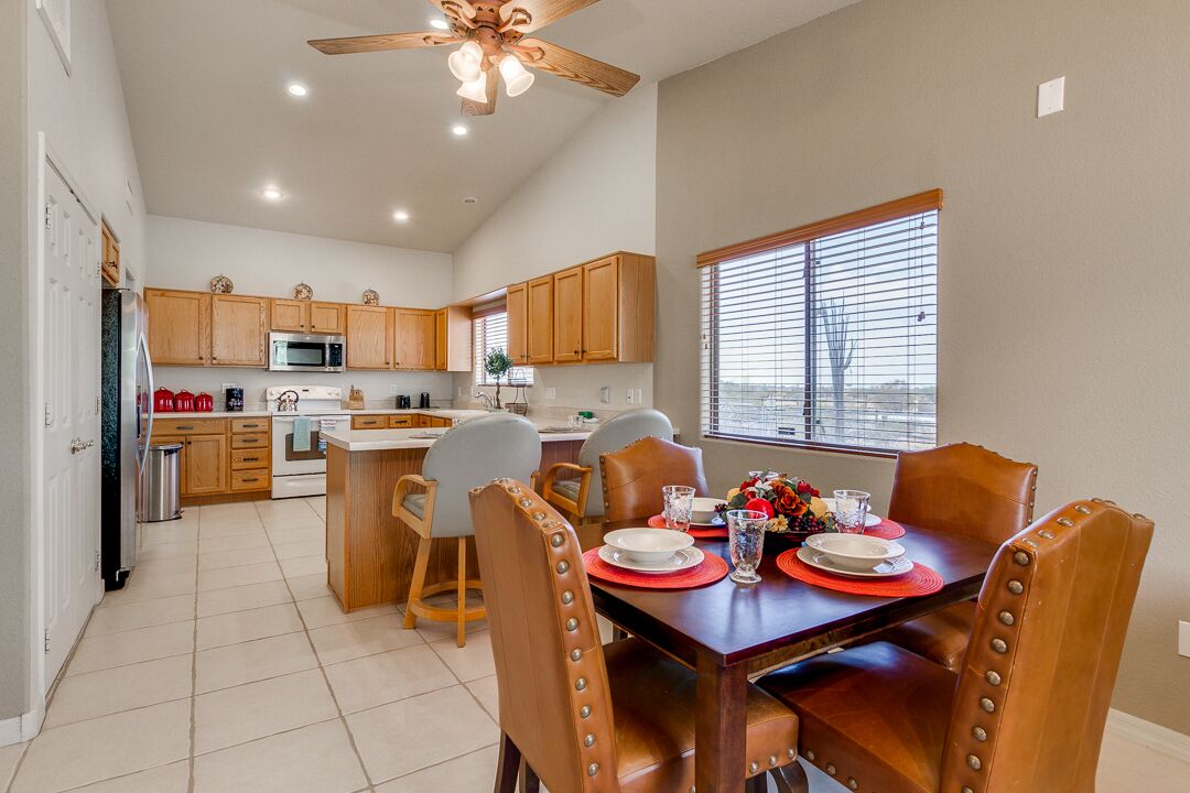 A spacious kitchen with wooden cabinets, a dining table set for four, and a ceiling fan.