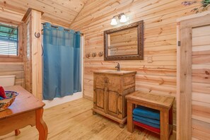 A wooden cabin bathroom with a wooden sink, a mirror, and a blue shower curtain.