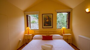 Une chambre d’hôtel avec un grand lit, deux lampes de chevet, un oreiller rouge et un tableau représentant la Joconde accroché au mur.
