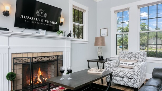 Una sala de estar moderna con chimenea, un televisor montado encima y un área de estar acogedora con un sillón estampado y un sofá.