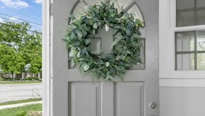 Una puerta principal gris con un adorno festivo y una ventana a la derecha.