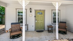 A house with a green door, two benches, and a small table with a wine glass.