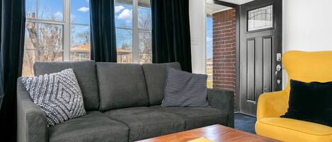 A living room with a grey sofa, a yellow armchair, and a wooden coffee table.