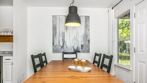 Un comedor con una mesa de madera, cuatro sillas, una lámpara colgante negra y un cuadro abstracto grande en la pared.