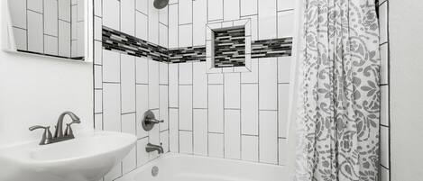 Un baño con lavamanos blanco, bañera y ducha con cabezal de lluvia.