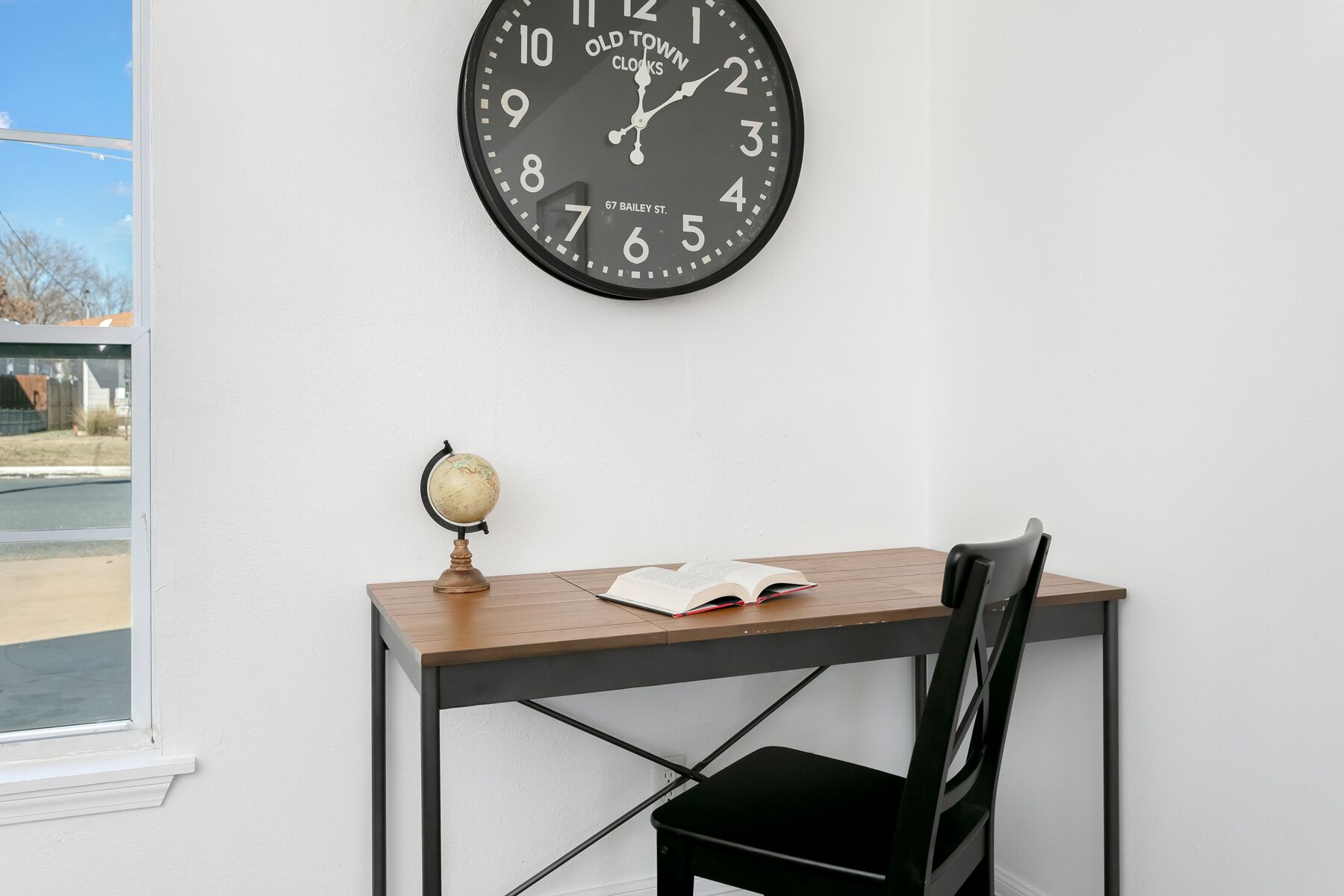 Une pièce avec un bureau en bois, une chaise noire, un globe terrestre et une horloge au mur.