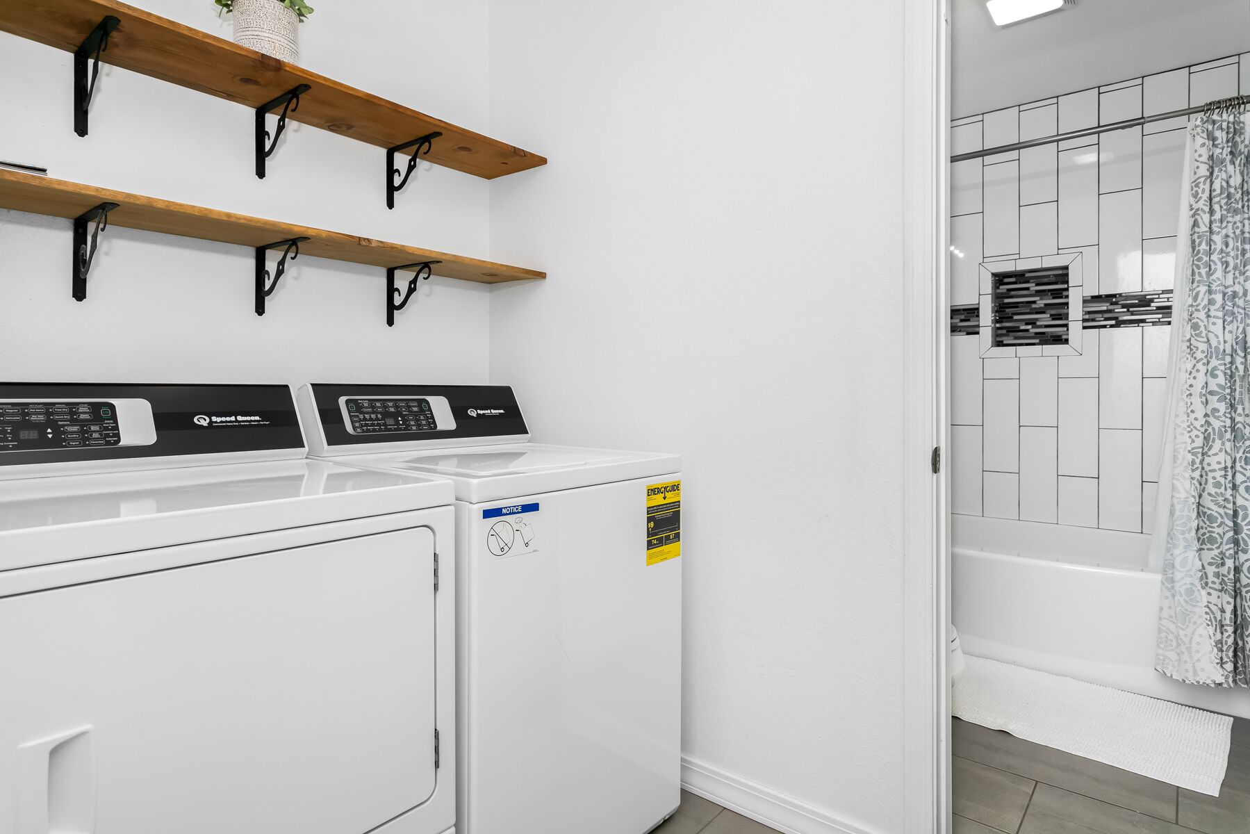 Un espace buanderie équipé de deux machines à laver, d’un étendoir et d’une zone douche avec une porte en verre.