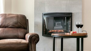 A leather armchair, a fireplace with a glass door, and a table with glasses and fruit. - Downtown Retreat Simply Unforgettable | Walk to Main | Shared Pool & Hot Tub (Fredericksburg)