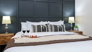 A neatly made bed with white linens, two bedside lamps, and a tray with glasses and fruit. - Downtown Retreat Simply Unforgettable | Walk to Main | Shared Pool & Hot Tub (Fredericksburg)