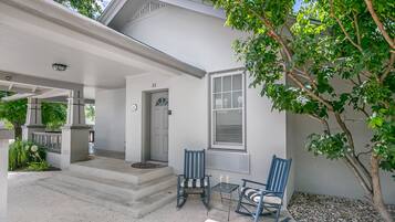 A white house with a covered porch, two rocking chairs, and a small table with two glasses.