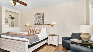 A bedroom with a wooden bed, bedside tables, a chair, a round table, and a ceiling fan.
