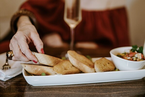 A person serving bread on a white plate with a small bowl of salad.