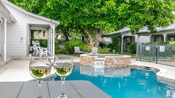 A swimming pool with a stone feature, surrounded by a covered patio area with chairs.