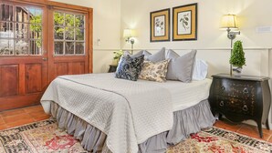 Un dormitorio con una cama, una mesita de noche, una lámpara, una puerta y dos cuadros en la pared.